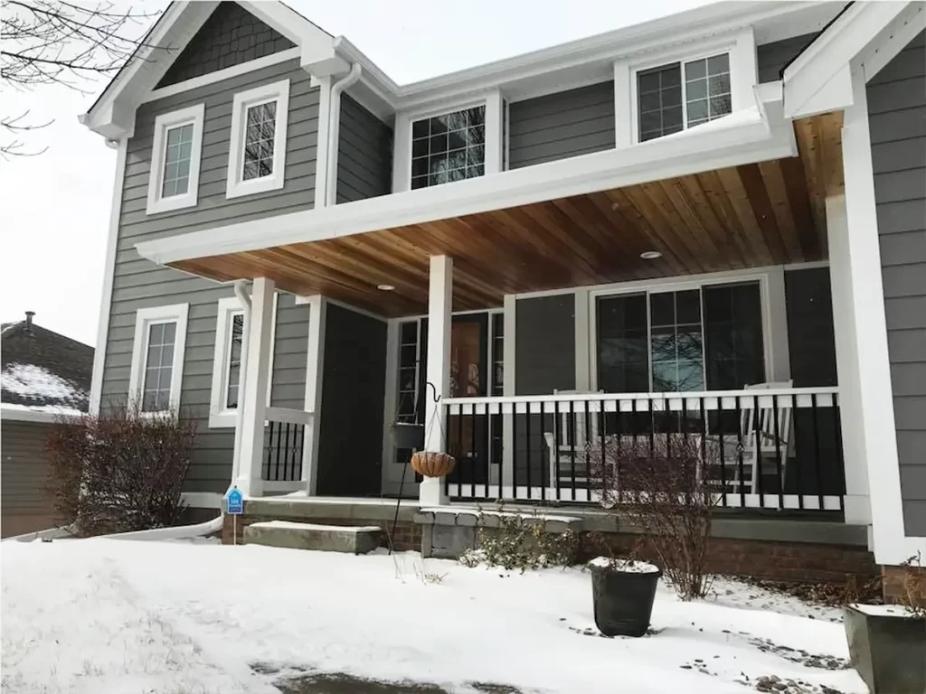 Two-story house with updated gray siding and a spacious front porch with a wood-paneled ceiling.