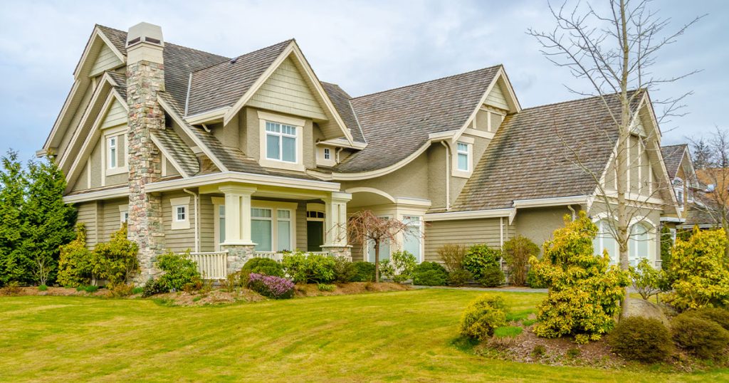 Luxury home exterior with stone chimney, wood siding, and well-maintained landscaping in suburban neighborhood