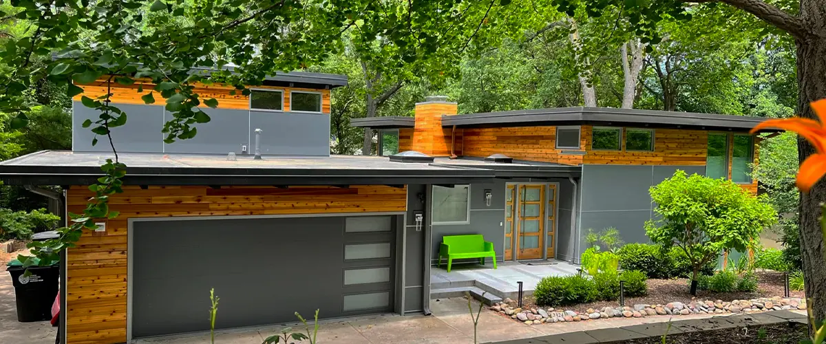Modern home exterior with cedar and gray siding surrounded by lush landscaping and mature trees