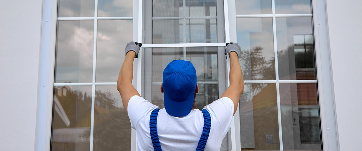 Background of blue-cap worker installing a mosquito net on large plastic window outside the building
