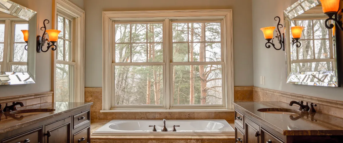 a bathroom with a large central window above a built-in bathtub, offering a view of a wooded area