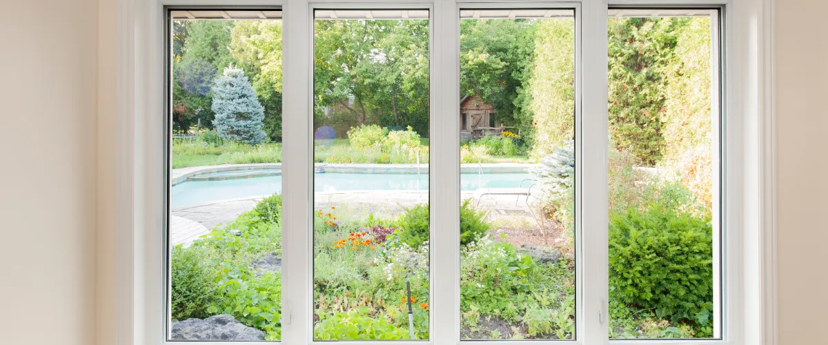 a set of four white-framed casement windows overlooking a lush garden and swimming pool