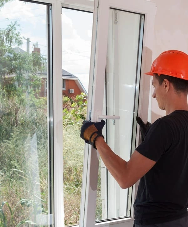 A contractor wearing an orange hard hat carefully fitting a white vinyl frame during a residential window replacement in Elkhorn, NE.