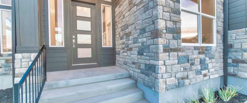 Close-up of vertical grey panel siding installed on a residential home near a white front door and concrete steps.