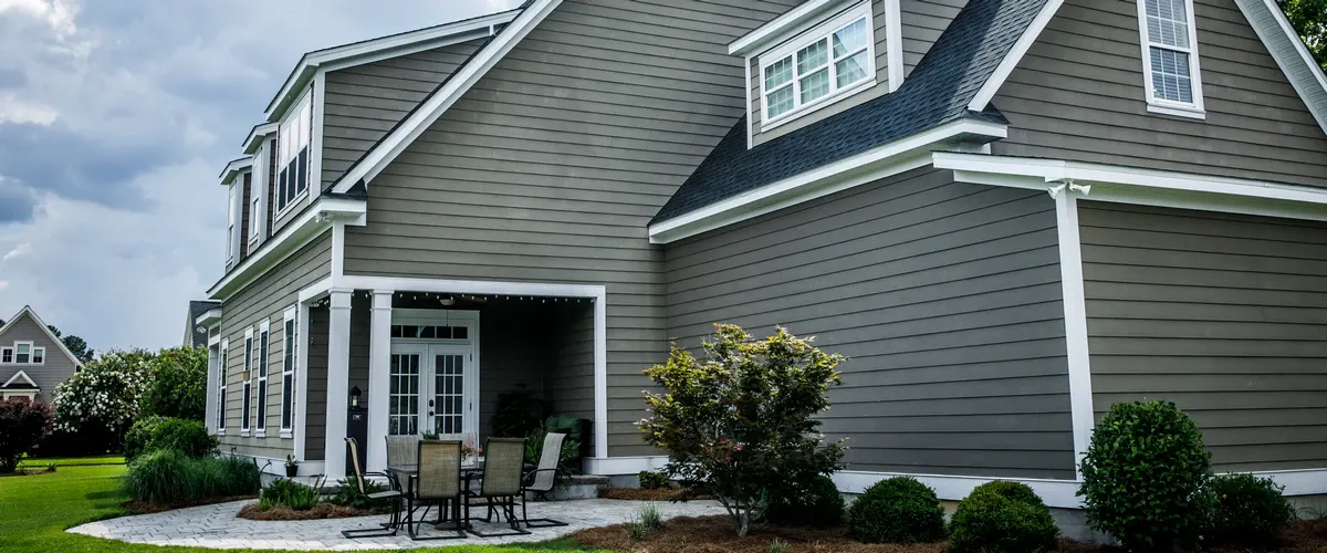 Wide shot of a residential backyard patio featuring a house with dark grey horizontal lap siding and white window trim.