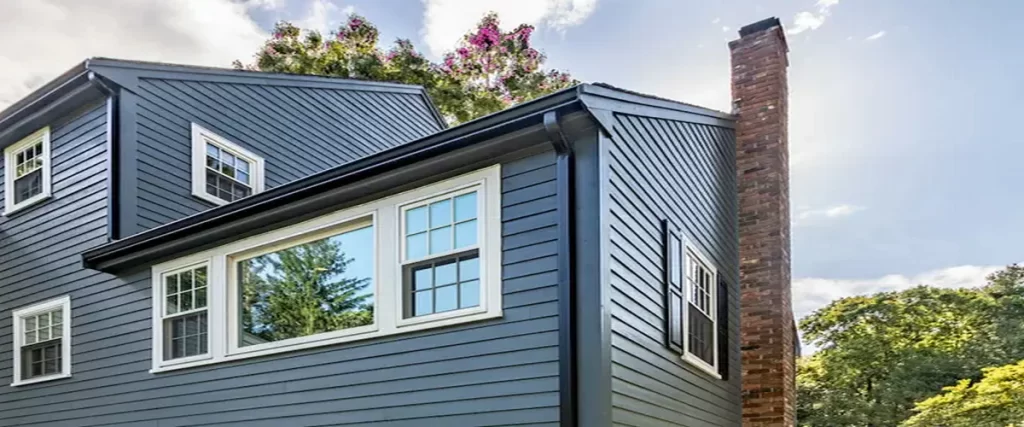 Exterior view of a dark blue residential house featuring clean soffit lines, window trim, and a brick chimney.