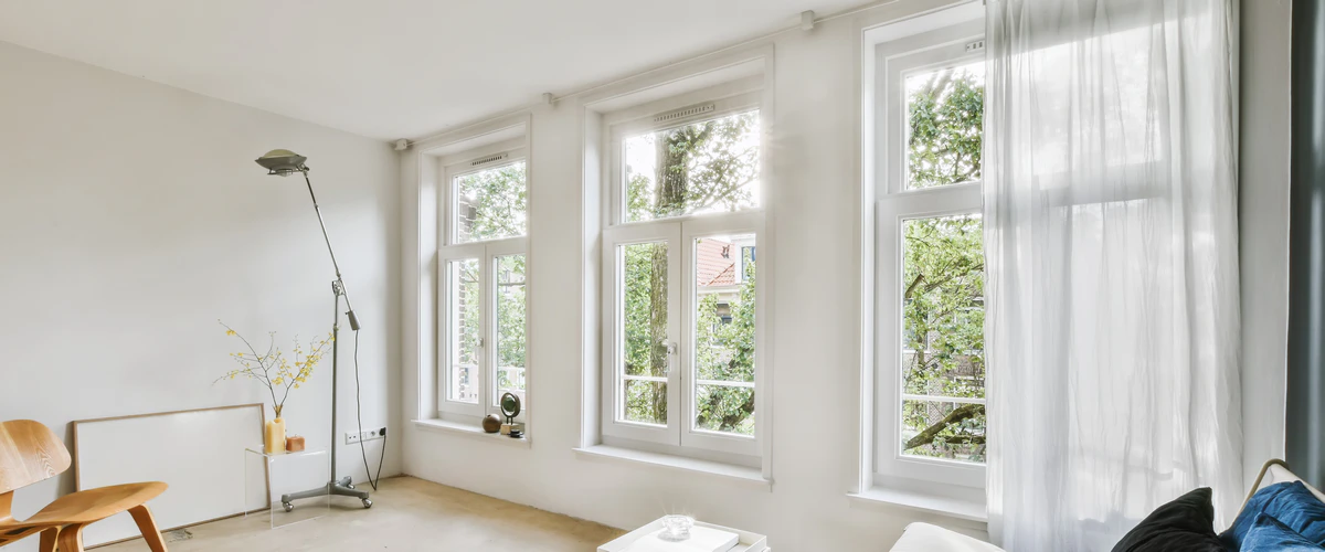 Interior view of three large white casement windows in a bright, minimalist living room with natural light.
