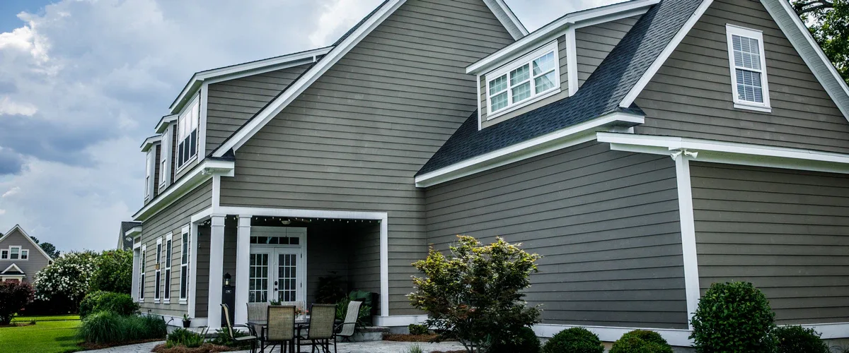 Exterior view of a large house showcasing grey horizontal lap siding, white window frames, and a cozy backyard patio area with outdoor seating.