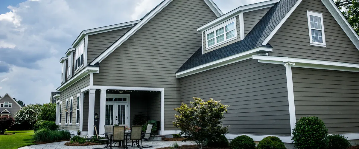 Rear exterior view of a house featuring grey-taupe horizontal siding, white decorative trim, and an outdoor patio area with white French doors.