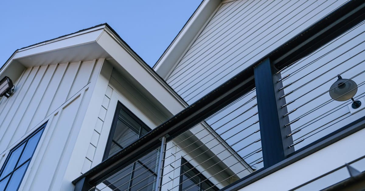 Close-up of James Hardie fiber cement siding in a white board and batten style featuring a modern cable balcony railing.