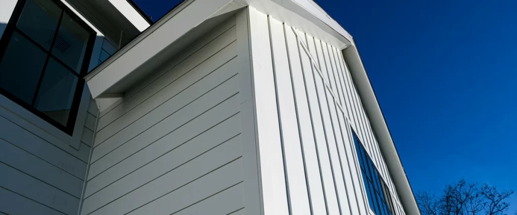 Detail shot of a home gable showing the clean lines of James Hardie white lap siding and vertical panels with black window frames.