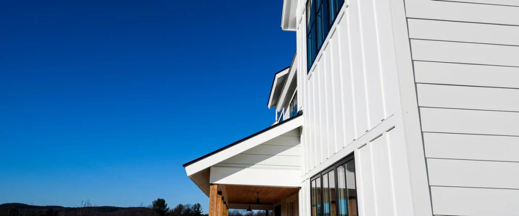 Low angle view of a house featuring James Hardie white board and batten vertical siding paired with horizontal lap siding under a bright blue sky.