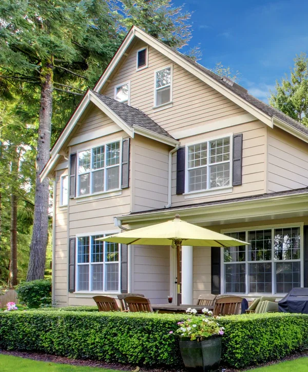 Exterior view of a Marvin window installation on a two-story beige craftsman home featuring classic black shutters and a patio with a yellow umbrella.