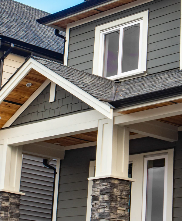 Close-up of a home exterior showing a fresh grey lap and shake siding replacement, featuring a covered porch with stone-base pillars and white trim in Ralston, NE.