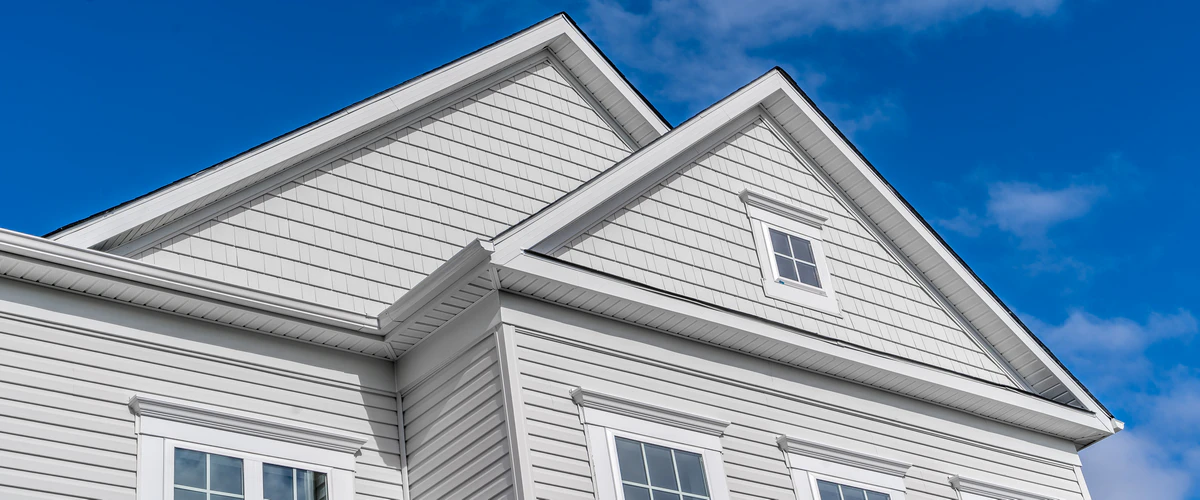 House exterior showing detailed light grey horizontal siding with matching shake-style siding on the upper roof gables, framed by bright white window trim.
