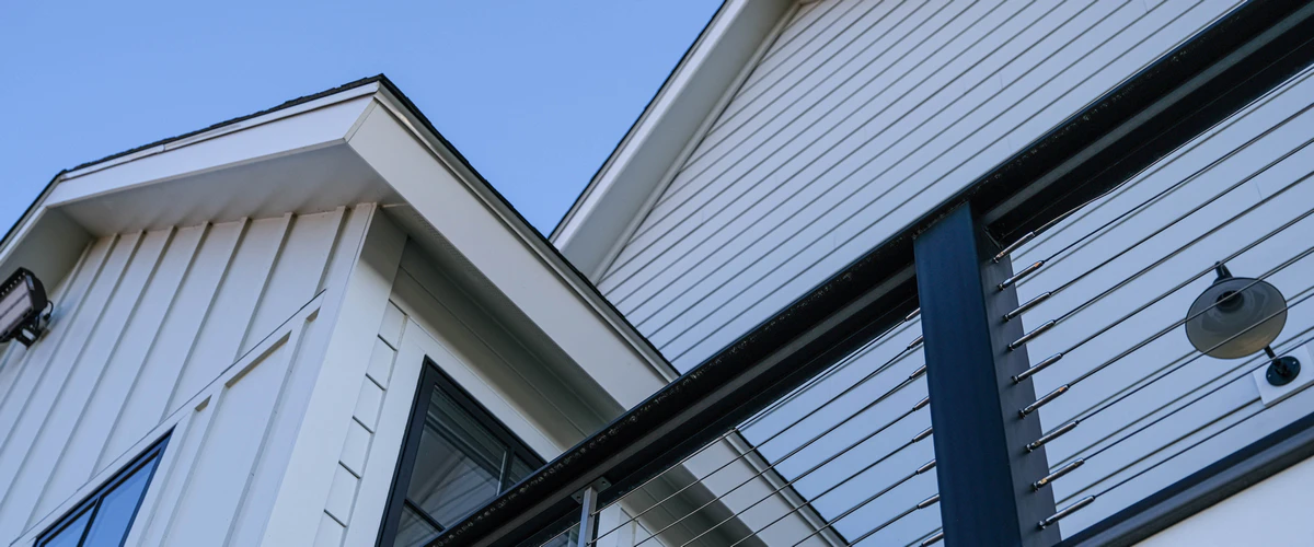 Low angle view of a modern home exterior featuring crisp white vertical board-and-batten siding alongside traditional horizontal siding, contrasted by black railings and window frames.