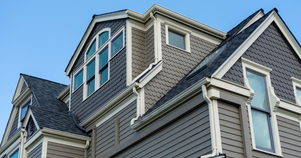 A multi-story home featuring a combination of grey horizontal lap siding and textured scalloped shingles with white trim, highlighting the results of an average cost siding installation.