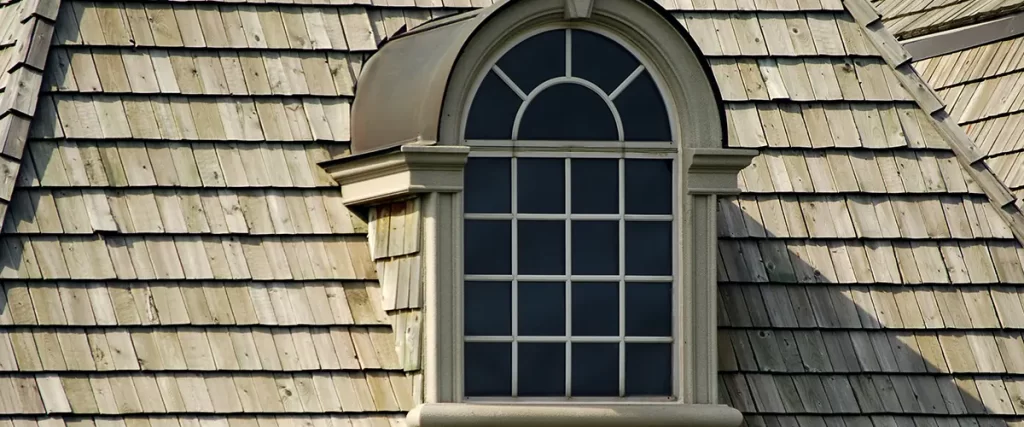 Arched dormer window with cedar shake roofing on a traditional luxury home exterior.