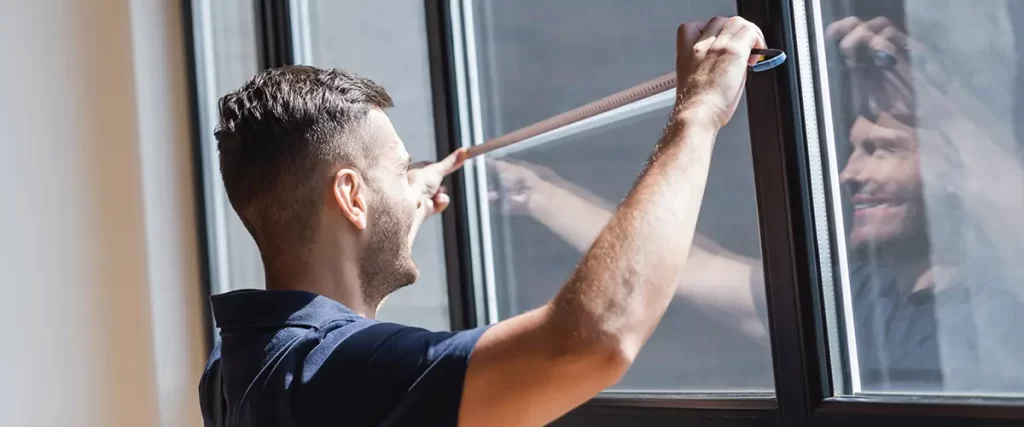 Technician measuring black framed replacement window for accurate installation.